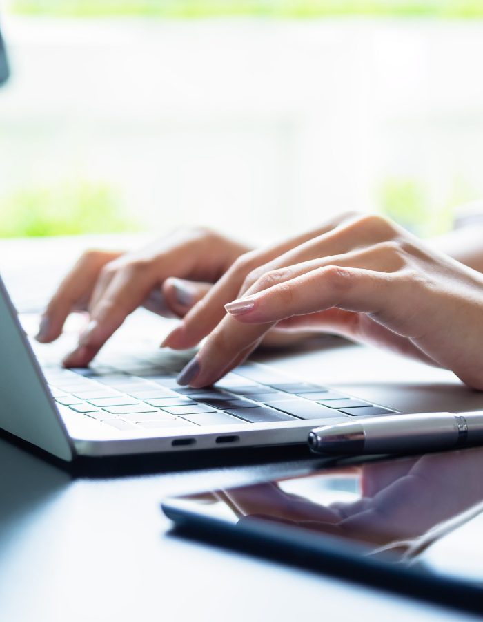 Close up hand of female typing on keyboard of laptop on table, working with technology device in modern office